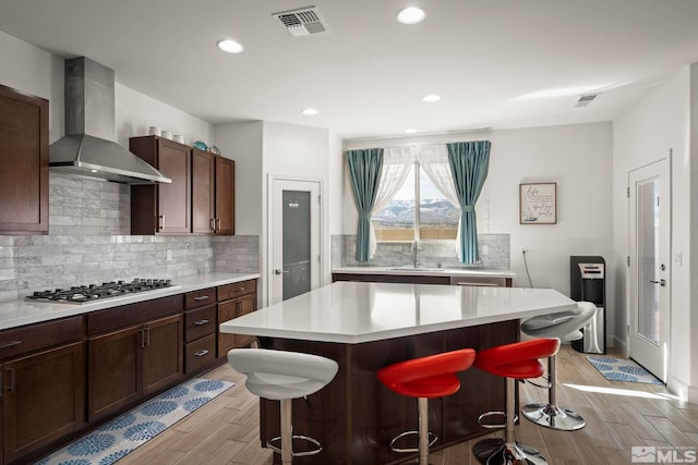 11223 Freedom Range Ln, Reno, NV 89521 - kitchen featuring stainless steel gas cooktop, wall chimney exhaust hood, a breakfast bar, a sink, and light countertops