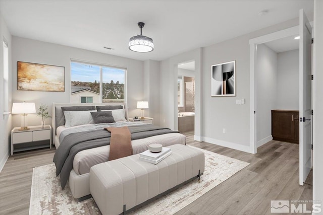 bedroom with baseboards, light wood-style flooring, and ensuite bath
