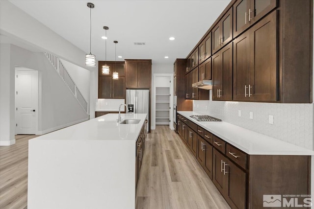 kitchen with a sink, light wood-style flooring, under cabinet range hood, dark brown cabinetry, and recessed lighting