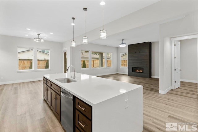 kitchen featuring a sink, dishwasher, light wood finished floors, baseboards, and pendant lighting