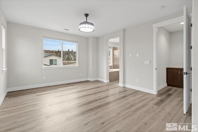 unfurnished bedroom with light wood-style flooring, baseboards, and connected bathroom