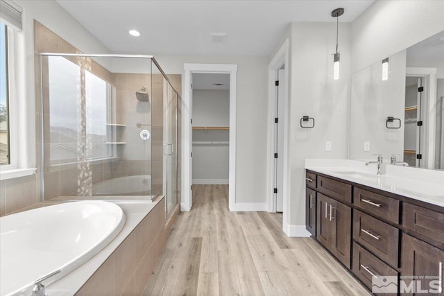 full bathroom featuring a stall shower, wood finished floors, a bath, vanity, and a spacious closet