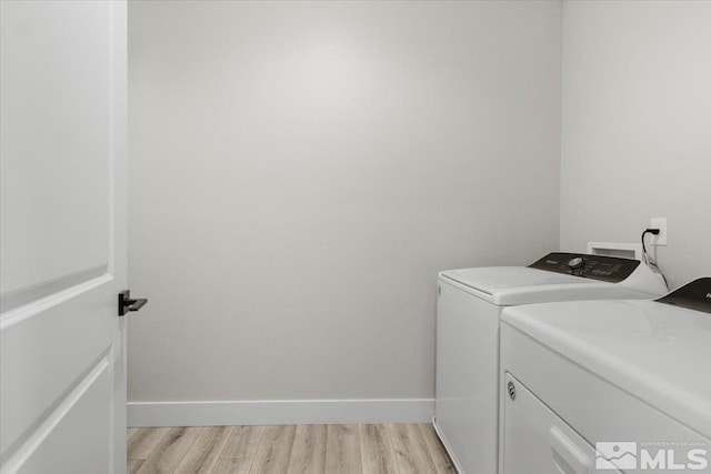 clothes washing area featuring separate washer and dryer, light wood finished floors, and baseboards