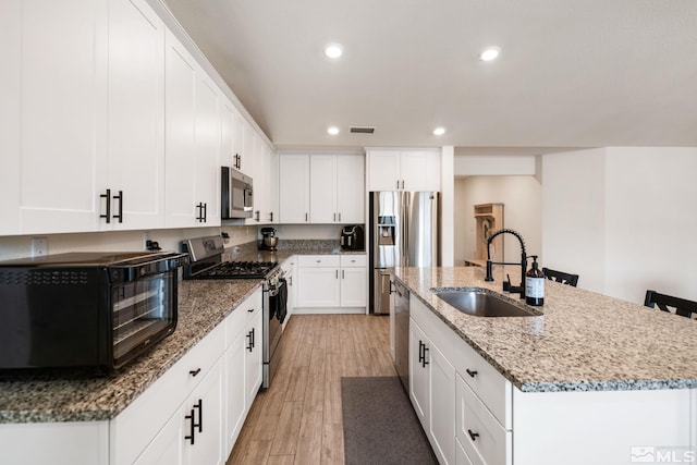 276 Greywall Ct, Dayton, NV 89403 - kitchen featuring appliances with stainless steel finishes, a sink, light wood-style flooring, a kitchen island with sink, and white cabinetry
