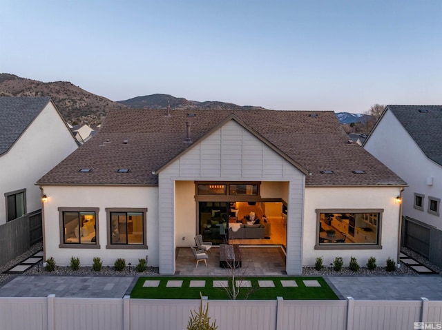back of property with a fenced front yard, a mountain view, and roof with shingles