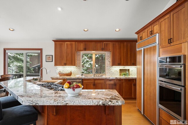 kitchen featuring stainless steel double oven, paneled built in refrigerator, brown cabinetry, a sink, and recessed lighting