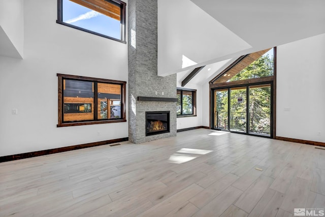 unfurnished living room featuring high vaulted ceiling, baseboards, a stone fireplace, and wood finished floors