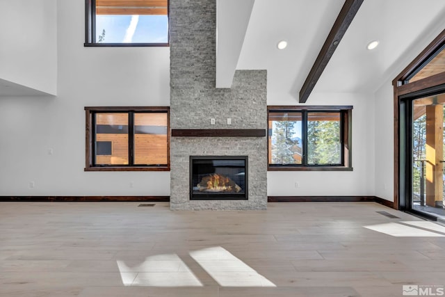 unfurnished living room with plenty of natural light, wood finished floors, a stone fireplace, baseboards, and recessed lighting