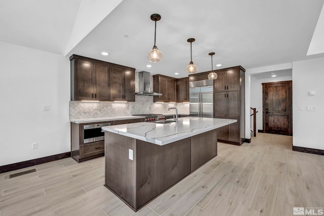 kitchen featuring appliances with stainless steel finishes, wall chimney exhaust hood, a sink, light wood-style flooring, and backsplash