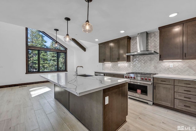 kitchen with wall chimney exhaust hood, luxury stove, a sink, decorative backsplash, and light stone countertops