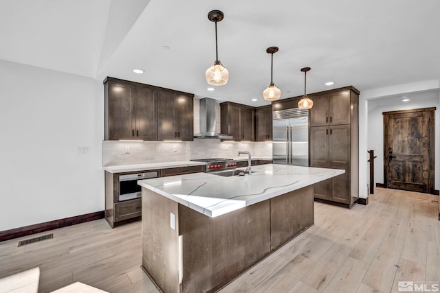 kitchen with wall chimney range hood, high quality appliances, light wood-style flooring, recessed lighting, and dark brown cabinets