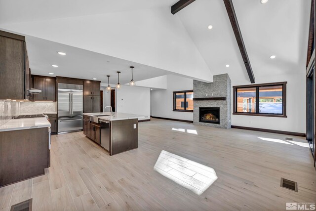 kitchen with stainless steel appliances, dark brown cabinetry, a sink, beamed ceiling, and baseboards