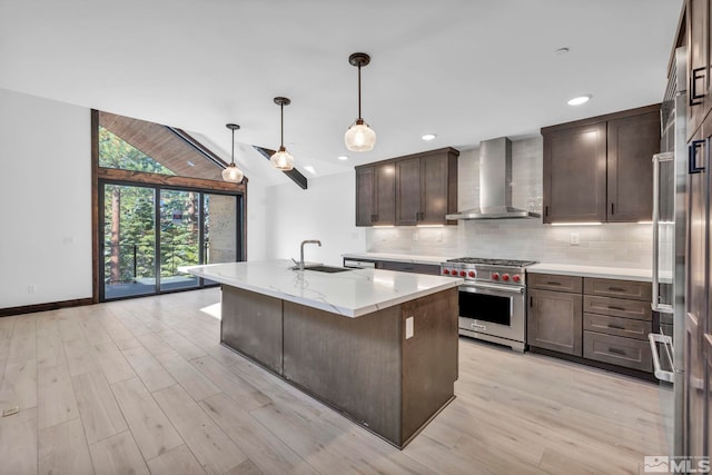 kitchen with premium stove, wall chimney range hood, a sink, light wood finished floors, and decorative backsplash