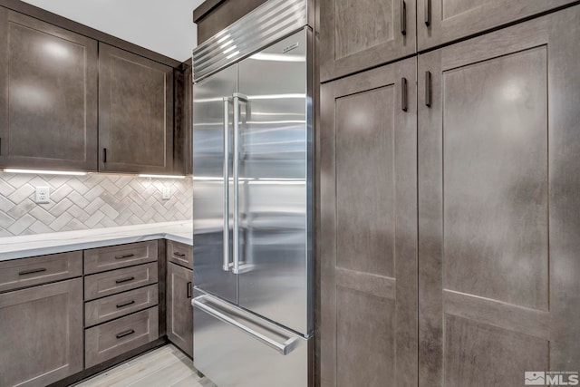 kitchen with built in refrigerator, tasteful backsplash, light countertops, and dark brown cabinets