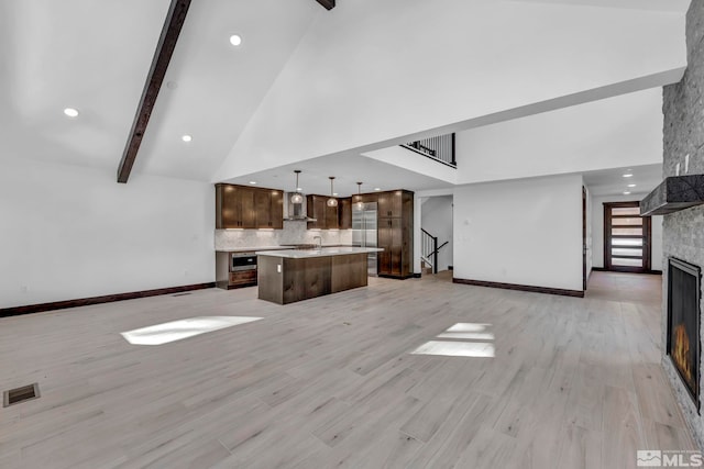 unfurnished living room with high vaulted ceiling, a large fireplace, baseboards, beamed ceiling, and light wood-type flooring