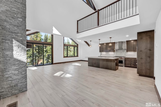 kitchen featuring high end range, open floor plan, wall chimney exhaust hood, a high ceiling, and light countertops
