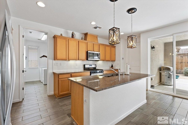 9820 Hafflinger Ln, Reno, NV 89521 - kitchen with stainless steel appliances, decorative backsplash, wood tiled floors, a center island with sink, and dark stone counters