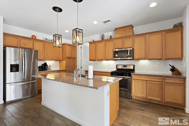 9820 Hafflinger Ln, Reno, NV 89521 - kitchen featuring appliances with stainless steel finishes, dark wood finished floors, a kitchen island with sink, light stone countertops, and brown cabinetry