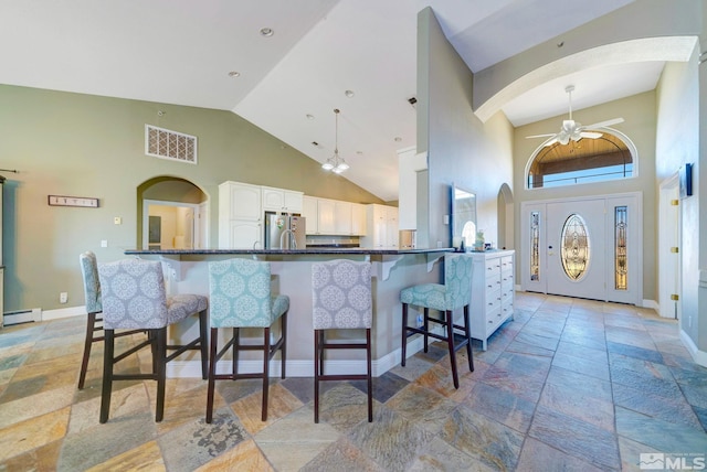 1253 Briggs Ln, Fallon, NV 89406 - kitchen with freestanding refrigerator, a baseboard heating unit, stone tile flooring, white cabinetry, and high vaulted ceiling