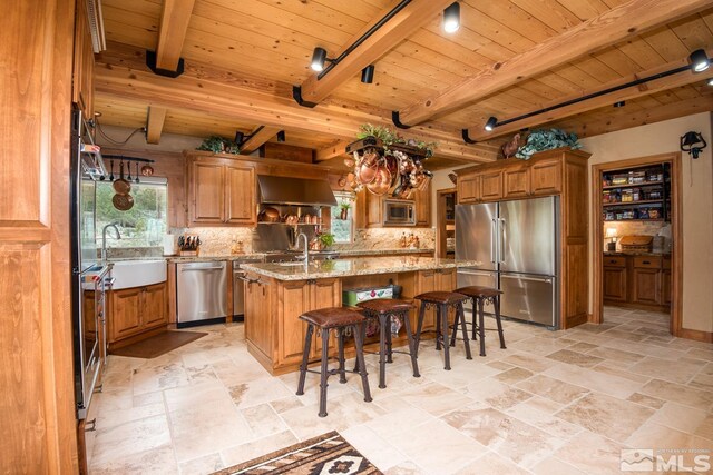 1101 Sierra Country Ct, Gardnerville, NV 89460 - kitchen featuring appliances with stainless steel finishes, a sink, wood ceiling, brown cabinets, and a center island with sink
