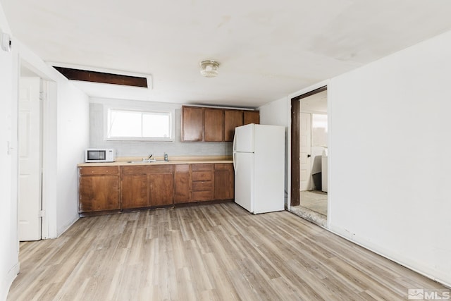 134 E 6th St, Battle Mountain, NV 89820 - kitchen with white appliances, light wood-type flooring, light countertops, a sink, and brown cabinetry