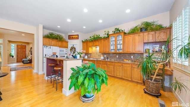 4940 Turning Leaf Way, Reno, NV 89519 - kitchen with light wood-style floors, a kitchen bar, backsplash, brown cabinetry, and recessed lighting