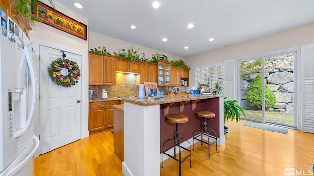 4940 Turning Leaf Way, Reno, NV 89519 - kitchen with white refrigerator with ice dispenser, light wood finished floors, a breakfast bar, brown cabinetry, and light stone countertops