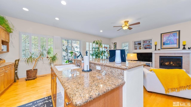 4940 Turning Leaf Way, Reno, NV 89519 - kitchen with light wood finished floors, a ceiling fan, a kitchen island, a tile fireplace, and light stone counters