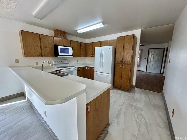 kitchen with white appliances, a sink, baseboards, and brown cabinets