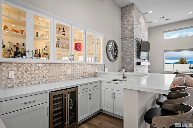 indoor bar with wine cooler, decorative backsplash, dark wood-style flooring, a towering ceiling, and recessed lighting