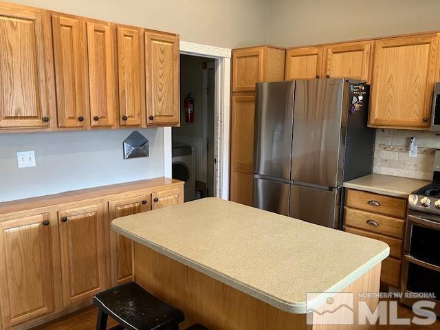 kitchen featuring appliances with stainless steel finishes, light countertops, a center island, backsplash, and washer / clothes dryer