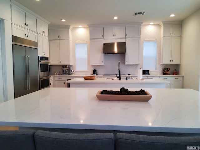 5449 Side Saddle Trl, Reno, NV 89511 - kitchen with appliances with stainless steel finishes, a center island with sink, wall chimney range hood, a sink, and white cabinetry