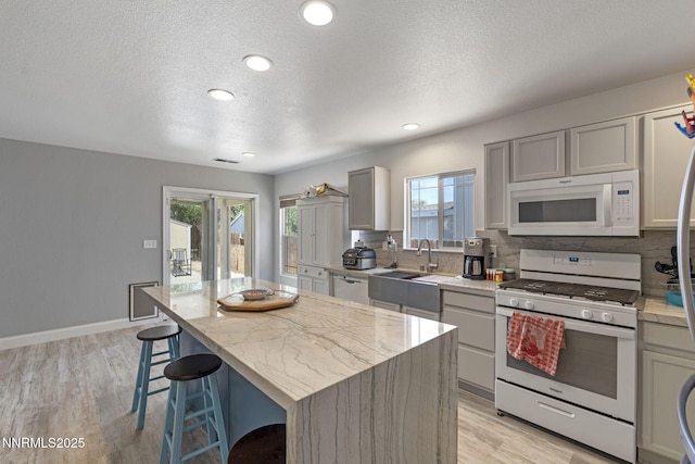 7721 Welsh Dr, Reno, NV 89506 - kitchen featuring white appliances, backsplash, light wood finished floors, a kitchen island, and a kitchen bar