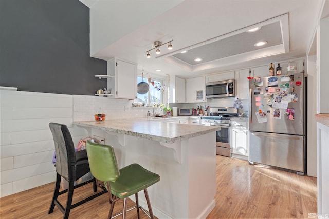 kitchen featuring stainless steel appliances, a peninsula, a raised ceiling, open shelves, and white cabinets