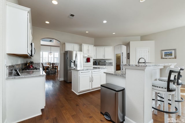 1659 Chiquita Ci, Minden, NV 89423 - kitchen featuring a kitchen island with sink, arched walkways, stainless steel appliances, dark wood-type flooring, and white cabinets