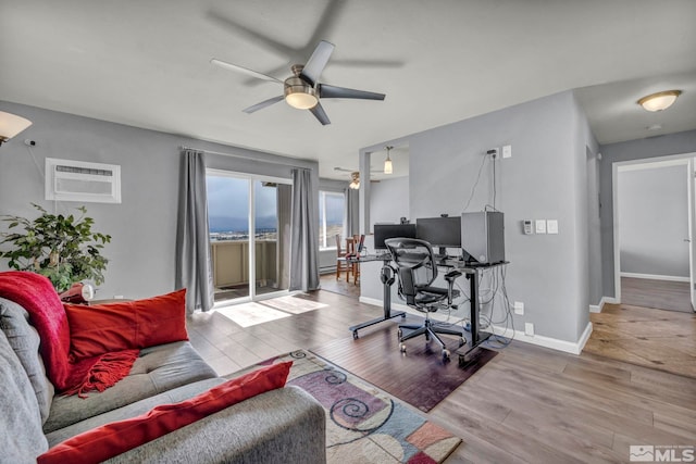 living room featuring a wall mounted AC, ceiling fan, an office area, wood finished floors, and baseboards