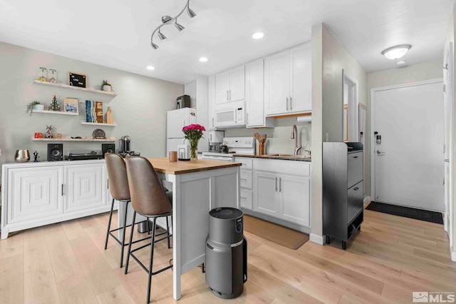 kitchen with white appliances, butcher block counters, a breakfast bar, light wood-style flooring, and white cabinets