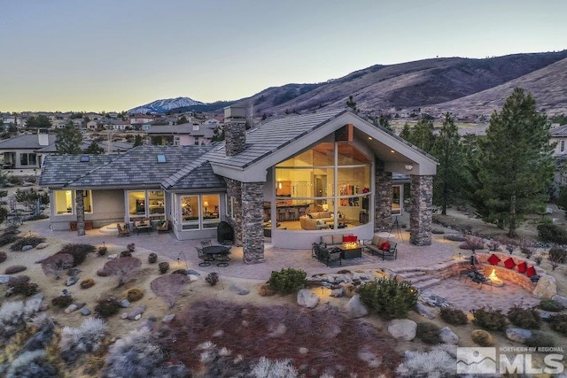 4020 Cocopah Ct, Reno, NV 89511 - back of house at dusk with a mountain view, a patio, an outdoor living space with a fire pit, a tiled roof, and stone siding