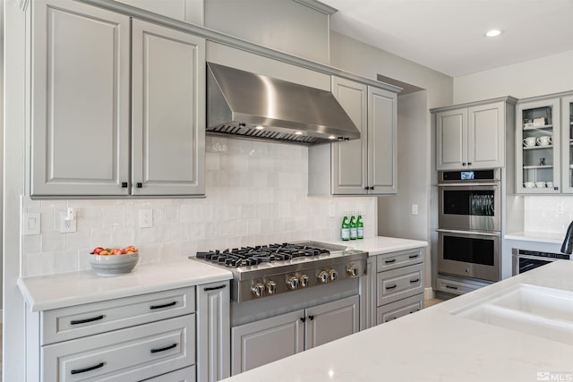 8956 Suncreek Trl, Reno, NV 89523 - kitchen with wall chimney exhaust hood, stainless steel appliances, gray cabinetry, backsplash, and light countertops