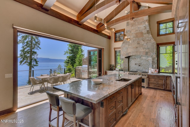 4250 N Lake Blvd, Carnelian Bay, CA 96140 - kitchen featuring beamed ceiling, brown cabinets, a kitchen island with sink, light wood finished floors, and light stone counters