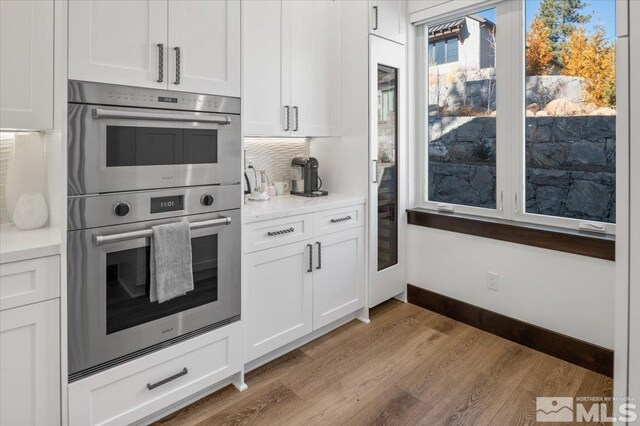 20765 Parc Foret Dr, Reno, NV 89511 - kitchen with stainless steel double oven, light wood finished floors, white cabinets, baseboards, and backsplash