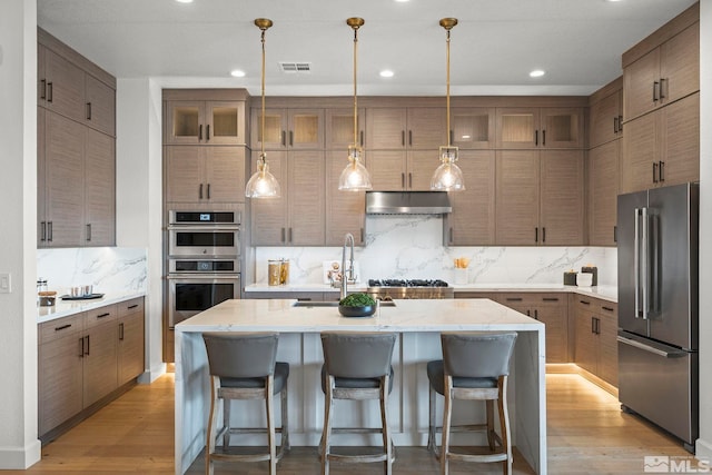 605 Braided Rope Dr, Reno, NV 89511 - kitchen featuring appliances with stainless steel finishes, a sink, backsplash, light wood-type flooring, and a center island with sink