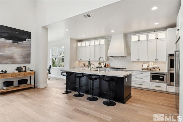 5192 Bordeaux Dr, Reno, NV 89511 - kitchen with custom exhaust hood, a kitchen breakfast bar, light wood finished floors, a sink, and white cabinets