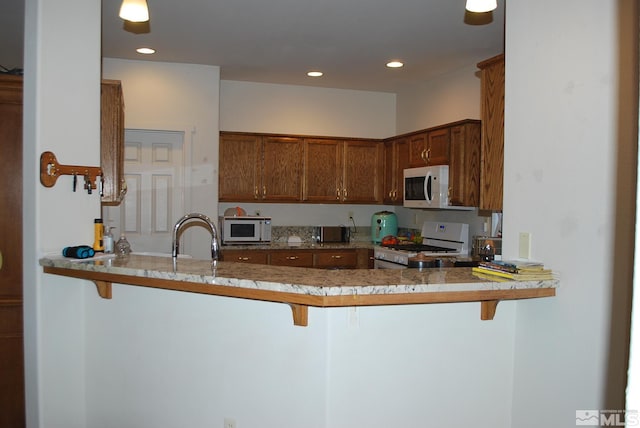 1075 Aster Ln, Fernley, NV 89408 - kitchen featuring white appliances, a peninsula, a sink, a breakfast bar, and recessed lighting