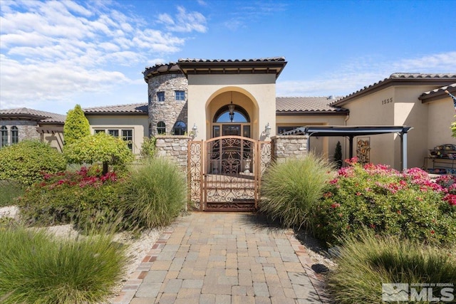 property entrance with stone siding, stucco siding, a gate, and a tile roof