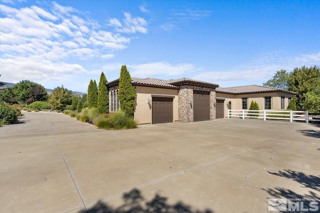 view of side of property featuring an attached garage, fence, driveway, stone siding, and stucco siding