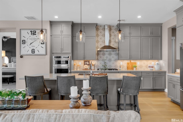 kitchen featuring gray cabinets, wall chimney exhaust hood, light countertops, a kitchen breakfast bar, and backsplash