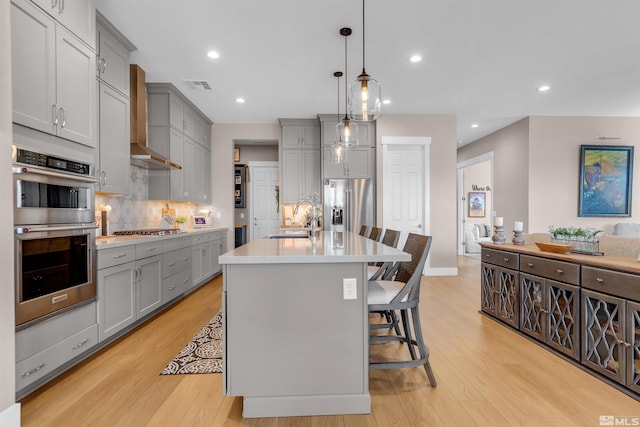 kitchen with gray cabinets, appliances with stainless steel finishes, a sink, wall chimney exhaust hood, and recessed lighting