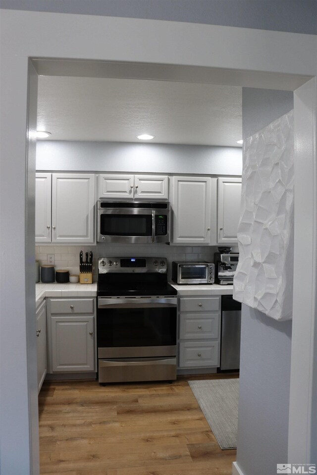 255 Ash St, Hawthorne, NV 89415 - kitchen featuring appliances with stainless steel finishes, decorative backsplash, white cabinetry, light wood-style flooring, and tile counters