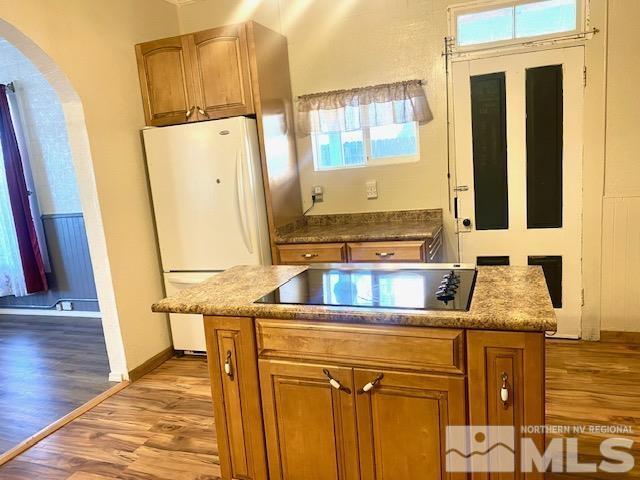 85 S Main, Paradise Valley, NV 89426 - kitchen with freestanding refrigerator, black electric cooktop, arched walkways, wood finished floors, and brown cabinets